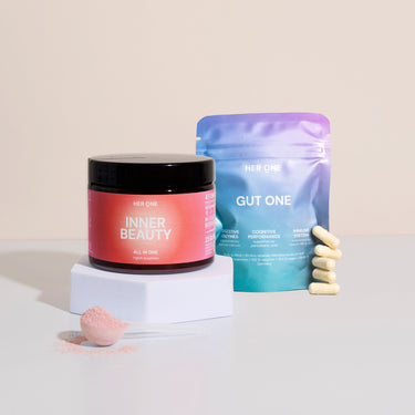 Tin of food supplements in pink tin and blue bag with capsules next to it on a white background.