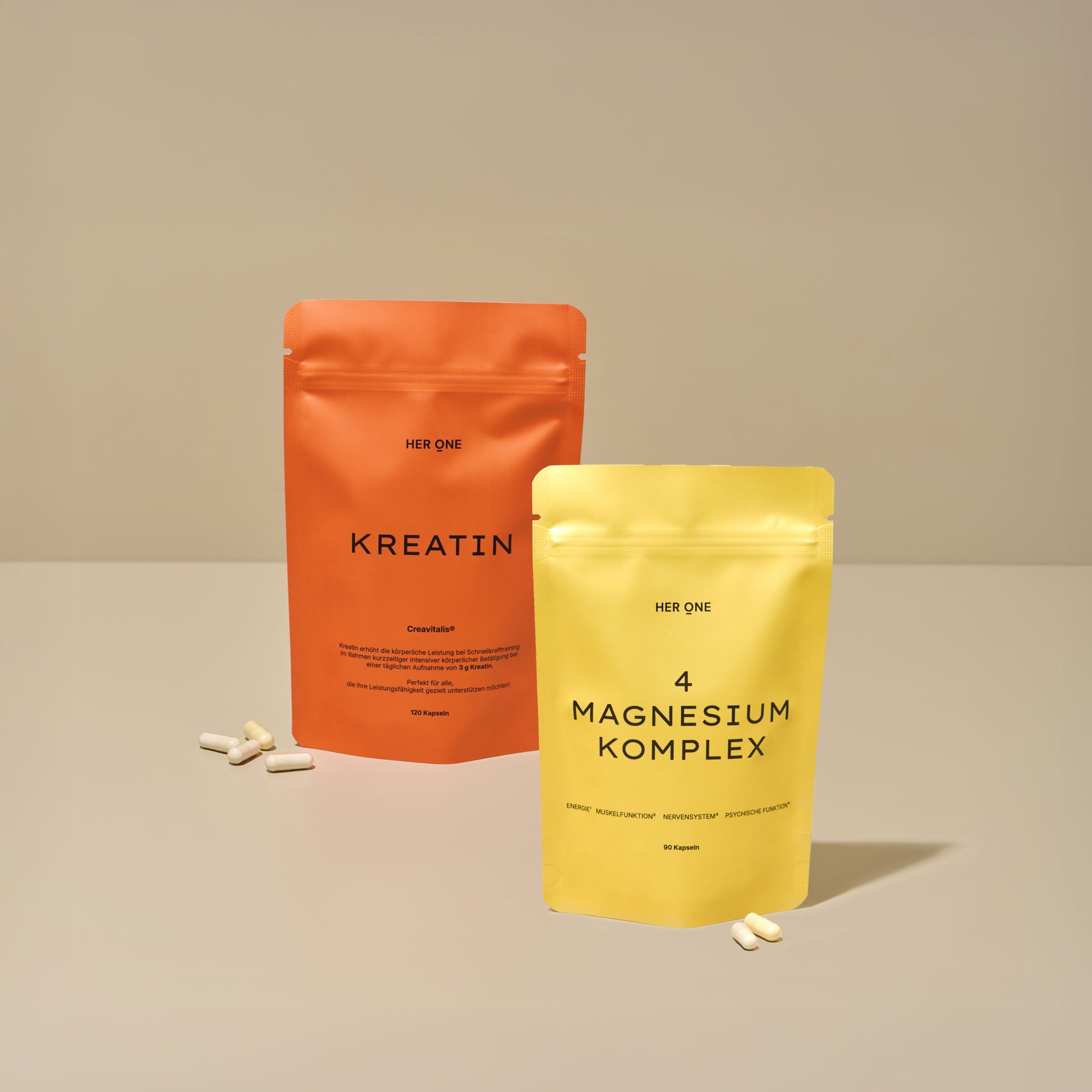 Two bags of food supplements, creatine in orange and magnesium complex in yellow, on a table with capsules.