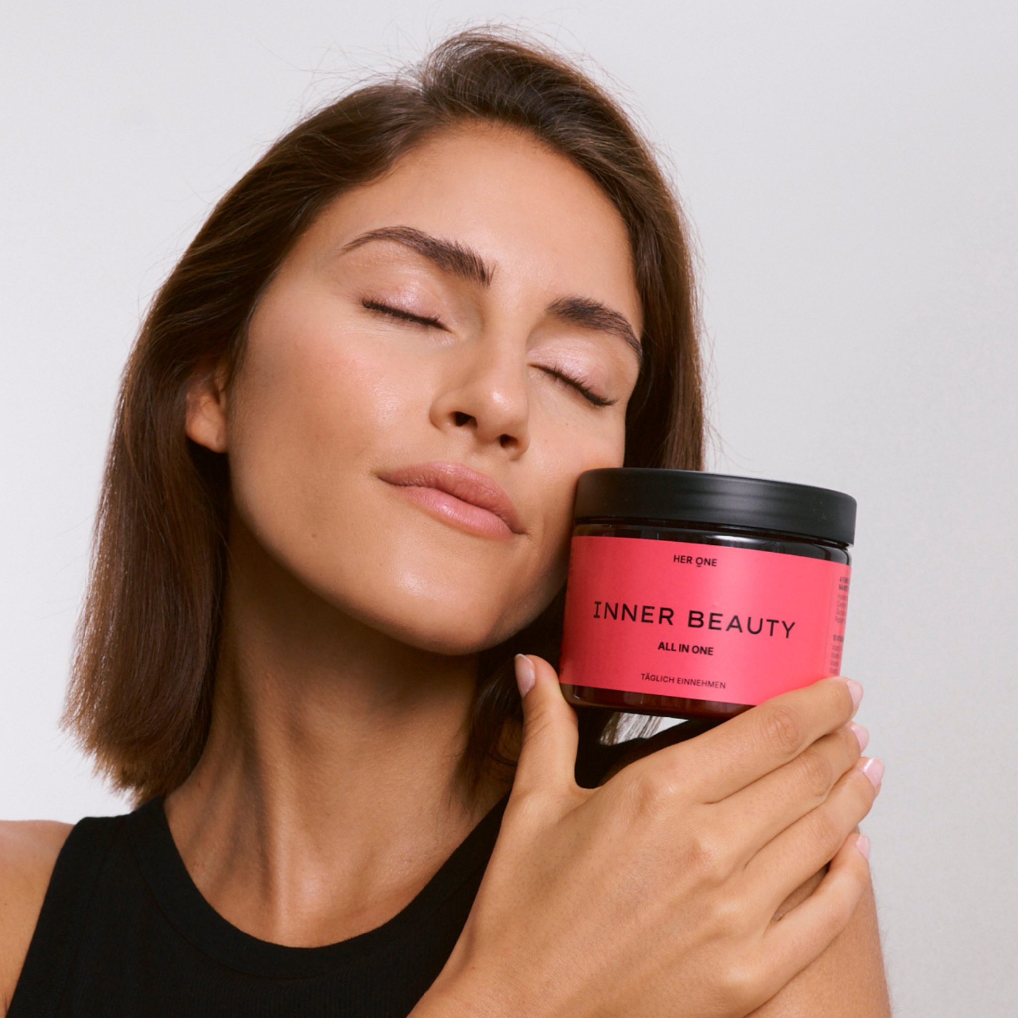 Woman holds HER ONE INNER BEAUTY to her cheek and closes her eyes in relaxation.