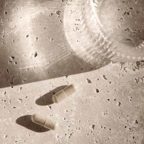 Two capsules and a glass stand on a structured surface in soft light.