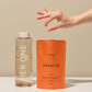 Hand holds a capsule over a packet of creatine and a bottle of water on a table.