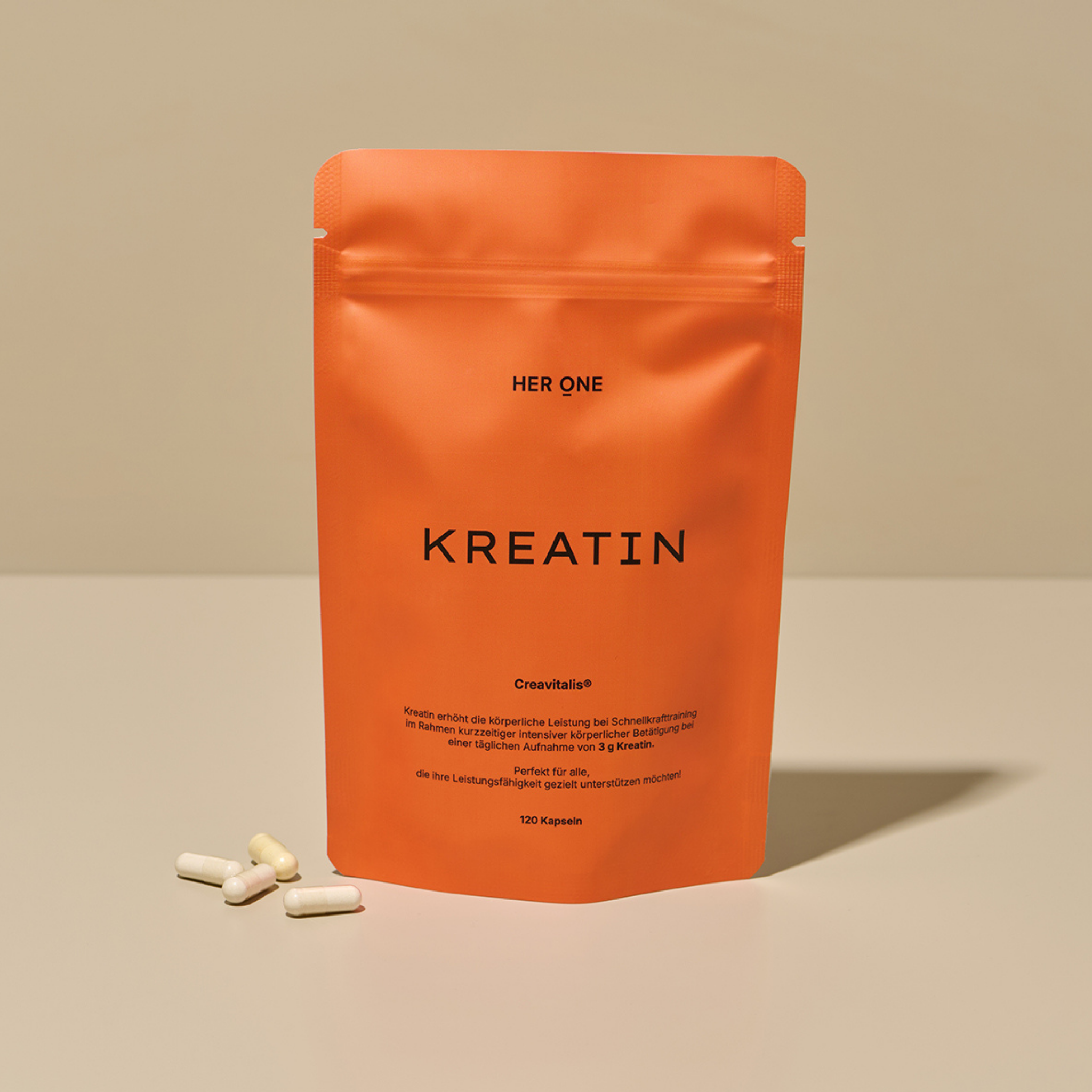 Orange pack labeled "Creatine" and white capsules lying next to it on a table.