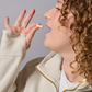 A person with curly hair holds a capsule in his hand and brings it to his mouth.