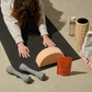 Person on yoga mat with fitness accessories: dumbbells, block, water bottle, foam roller and creatine powder.