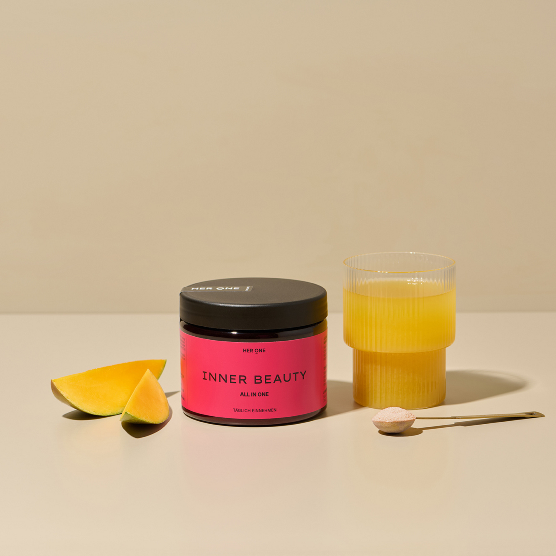 A glass with a yellow drink, a pink container withInner Beauty", a spoonful of powder and two pieces of mango.