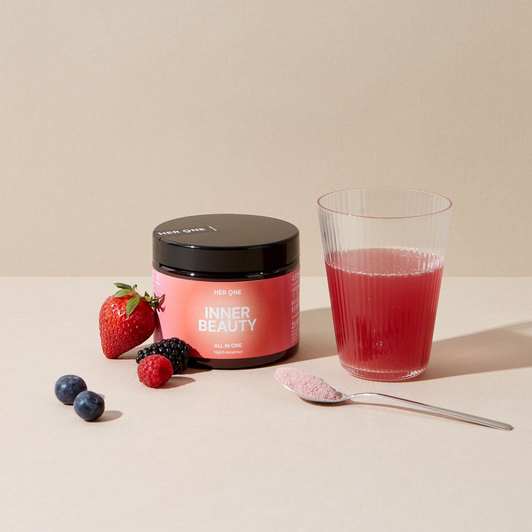 A glass of red drink, a container of Inner Beauty powder and berries on a table.