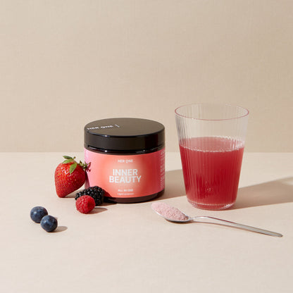 A glass of red drink, a container ofInner Beauty" powder and berries on a table.