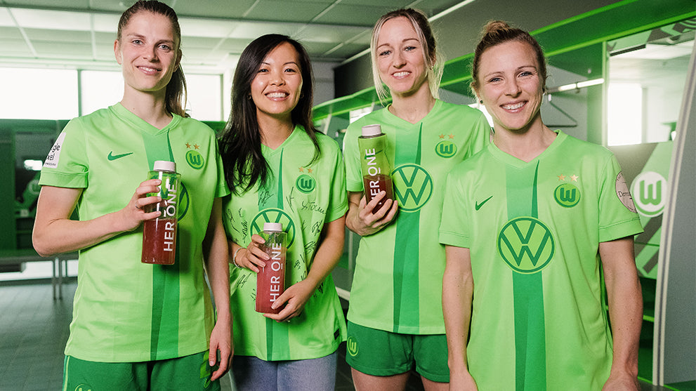 Four people in green jerseys hold plastic bottles in their hands and smile at the camera.