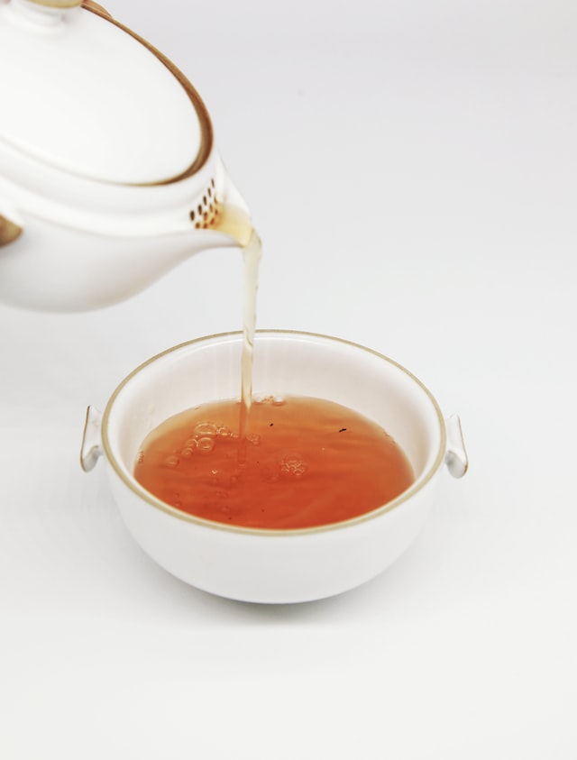 A white teapot is poured into a white bowl on a white background.
