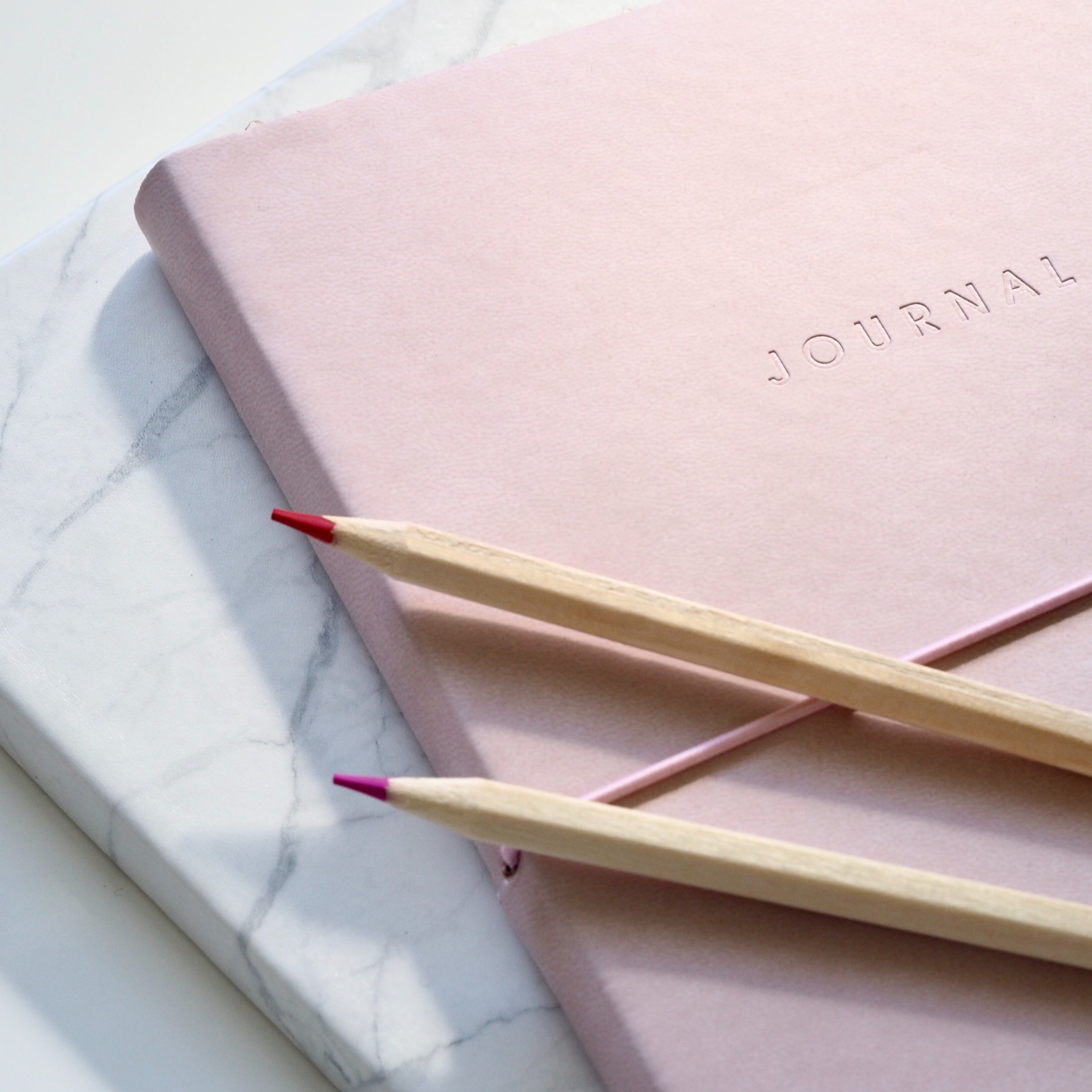 Two pencils on a pink journal and a marble-patterned background.