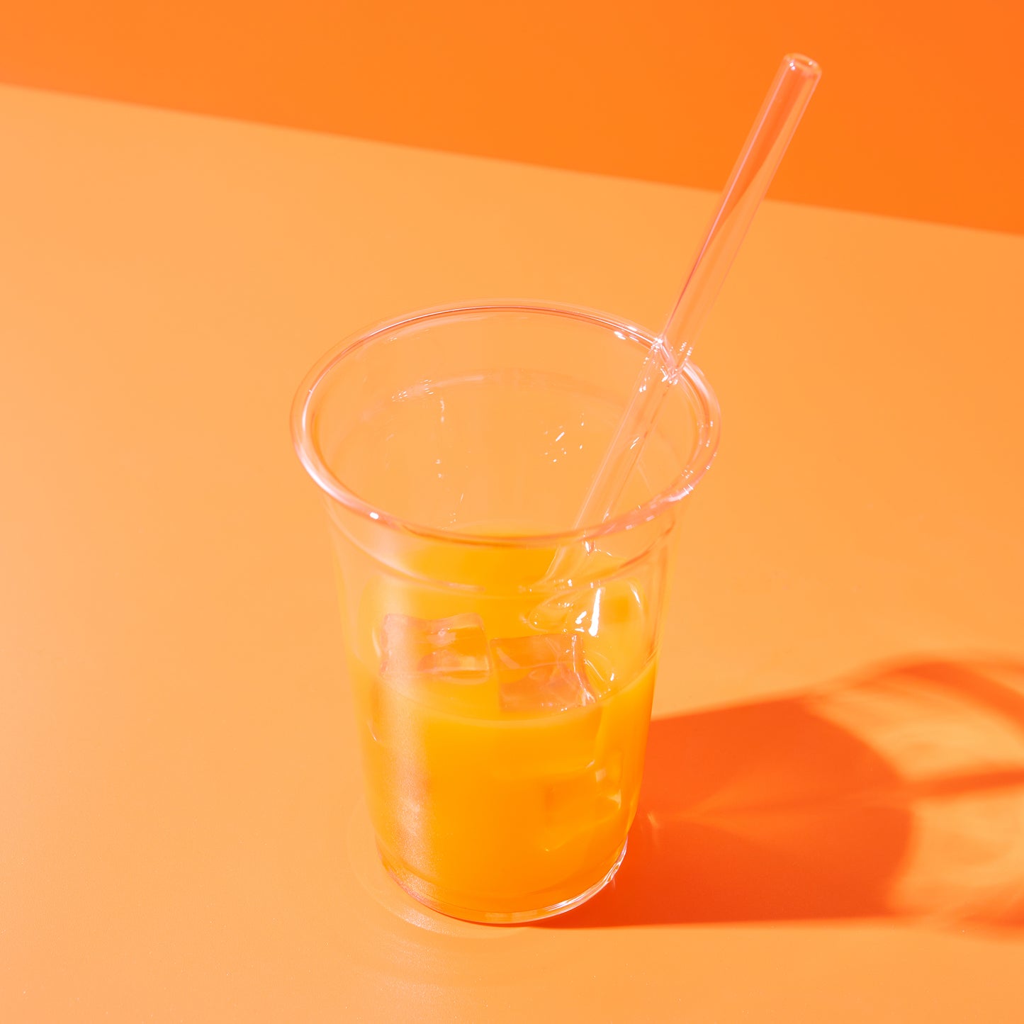 Un gobelet en plastique avec du jus d'orange et des glaçons sur un fond orange.