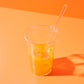 Un gobelet en plastique avec du jus d'orange et des glaçons sur un fond orange.