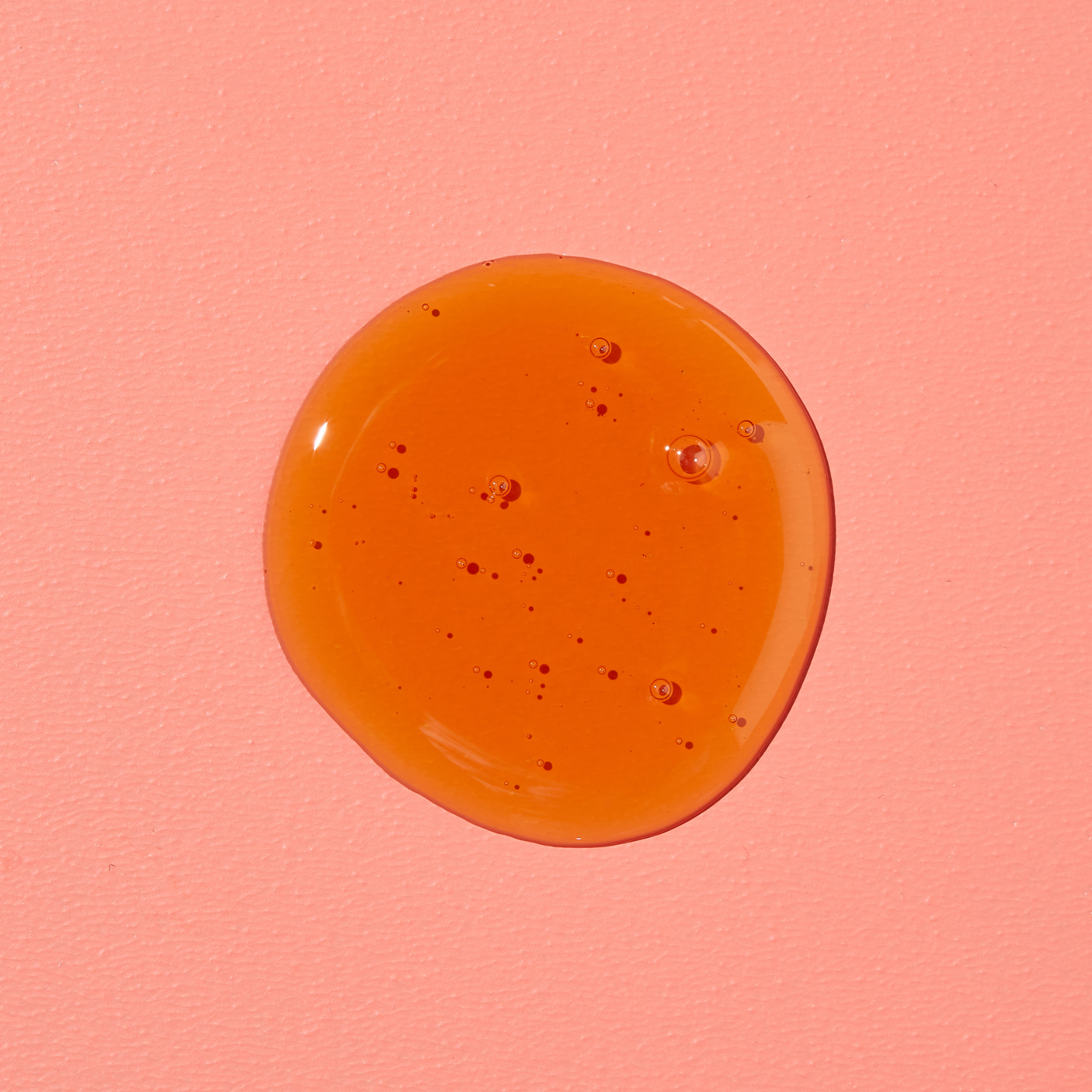 Un liquide orange rond avec des bulles sur fond rose.
