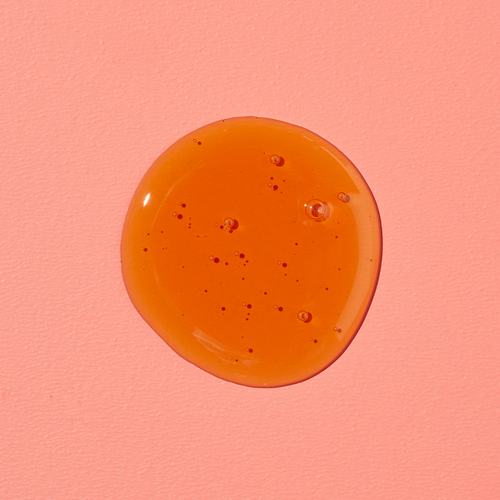 Un liquide rond et orange avec des bulles sur un fond rose.