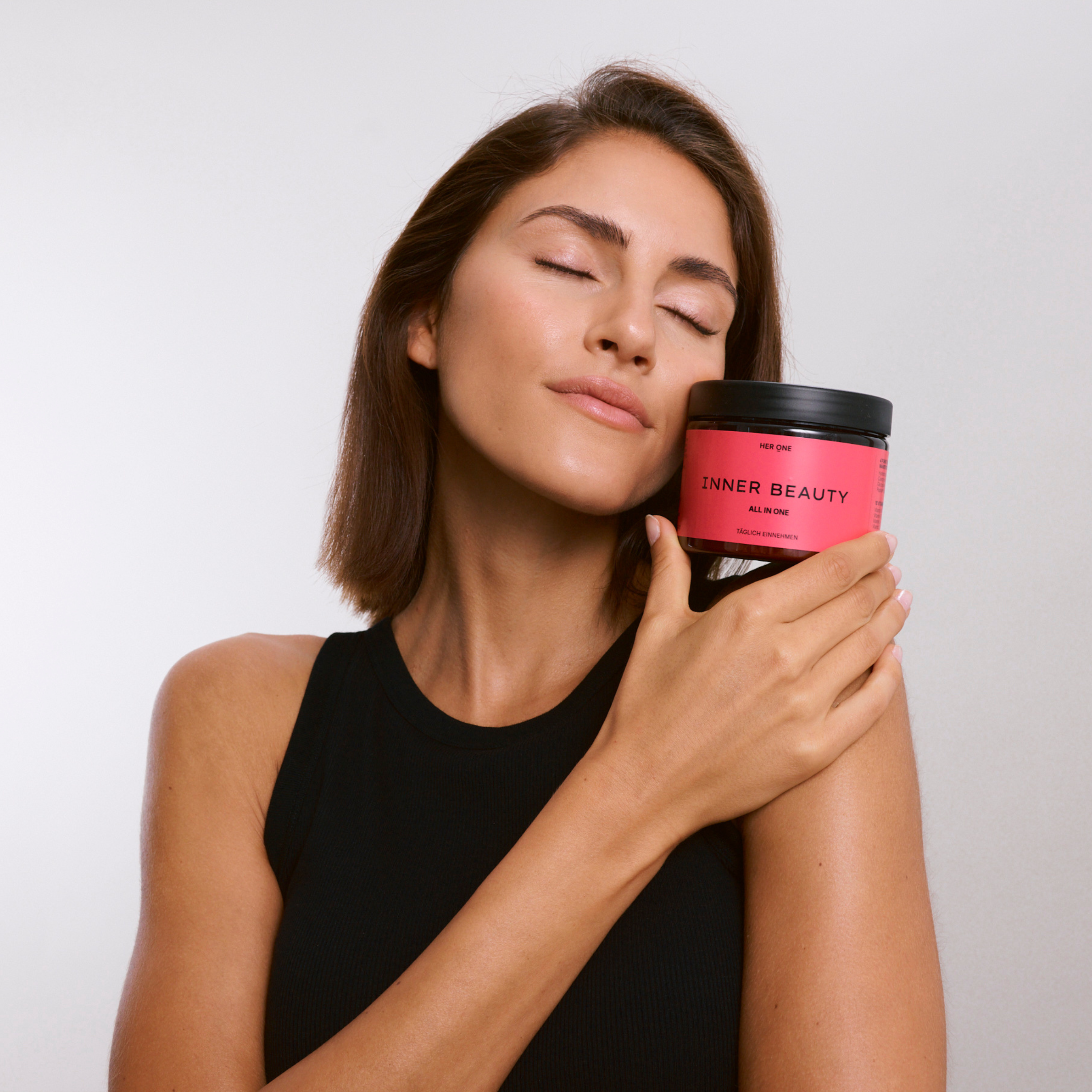 Femme tenant une boîte Inner Beauty contre son visage, fond rose, évoque le bien-être et la santé.