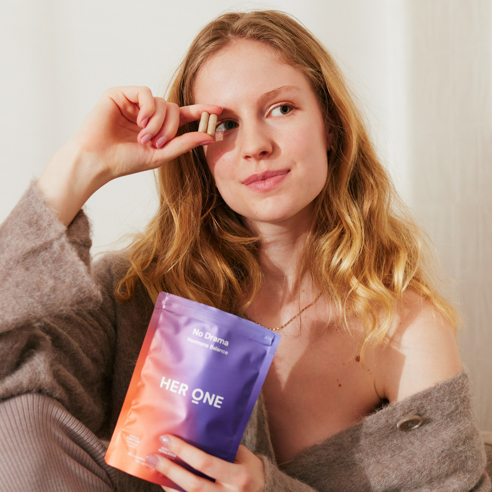 Une femme tient deux capsules et un sac portant l'inscription "HER ONE".