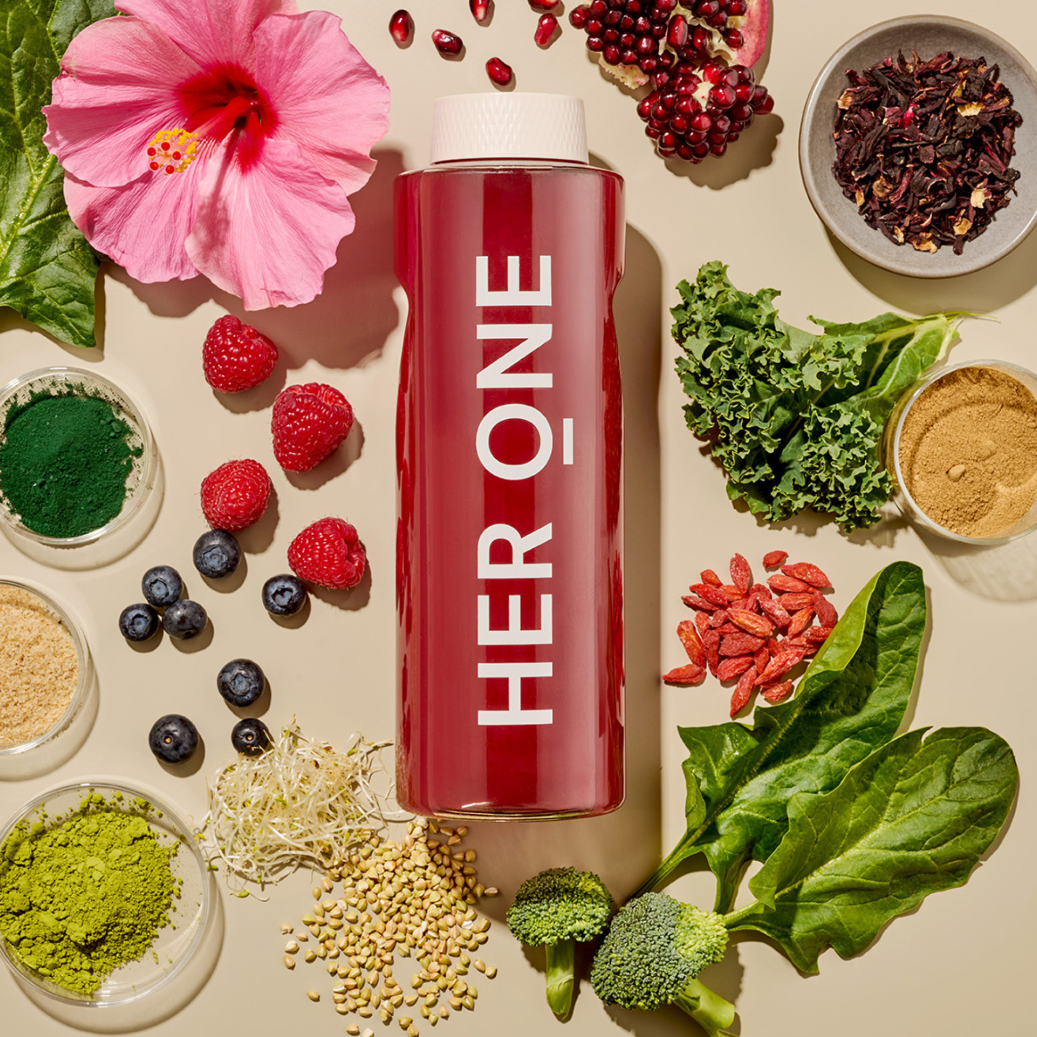 Une bouteille rouge avec l'inscription "HERONE" entourée d'ingrédients à base de fruits et de légumes sur un fond clair.