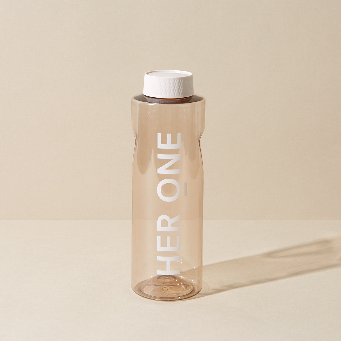 Borraccia trasparente con coperchio bianco e scritta "HER ONE" su sfondo beige.