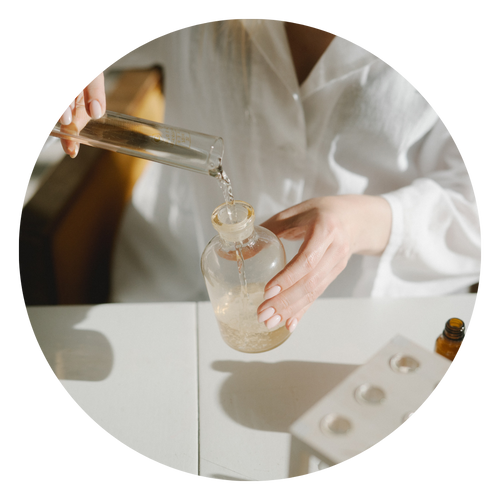 Una persona in camice bianco versa del liquido da un cilindro graduato in una beuta rotonda.