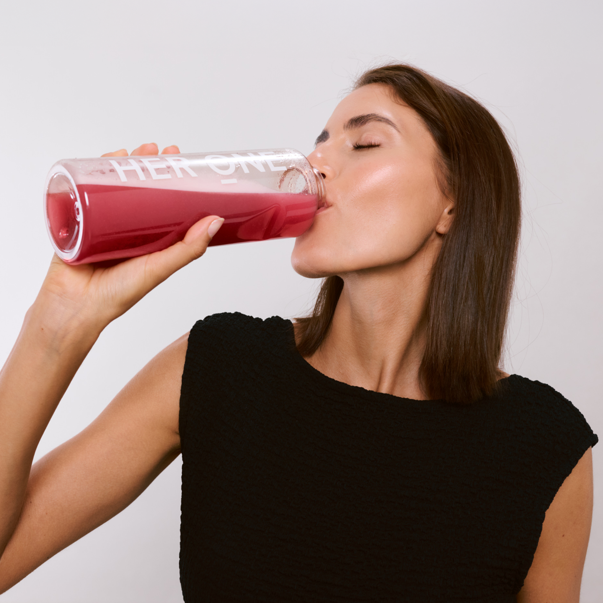 Una donna beve una bevanda rossa dalla bottiglia HER ONE e chiude gli occhi soddisfatta.