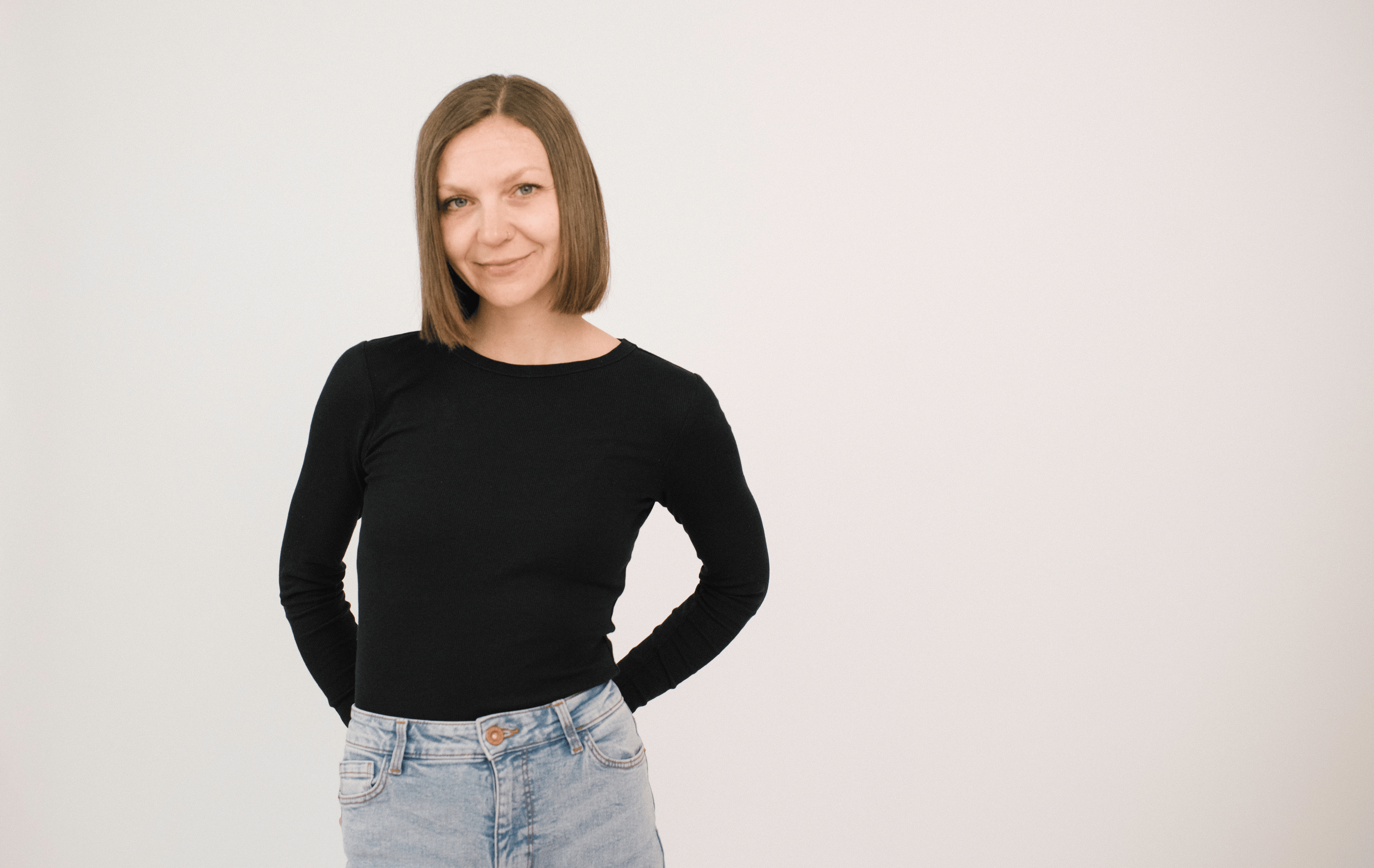 Una donna con i capelli lunghi fino alle spalle indossa un top nero e dei jeans e sorride dolcemente alla telecamera.