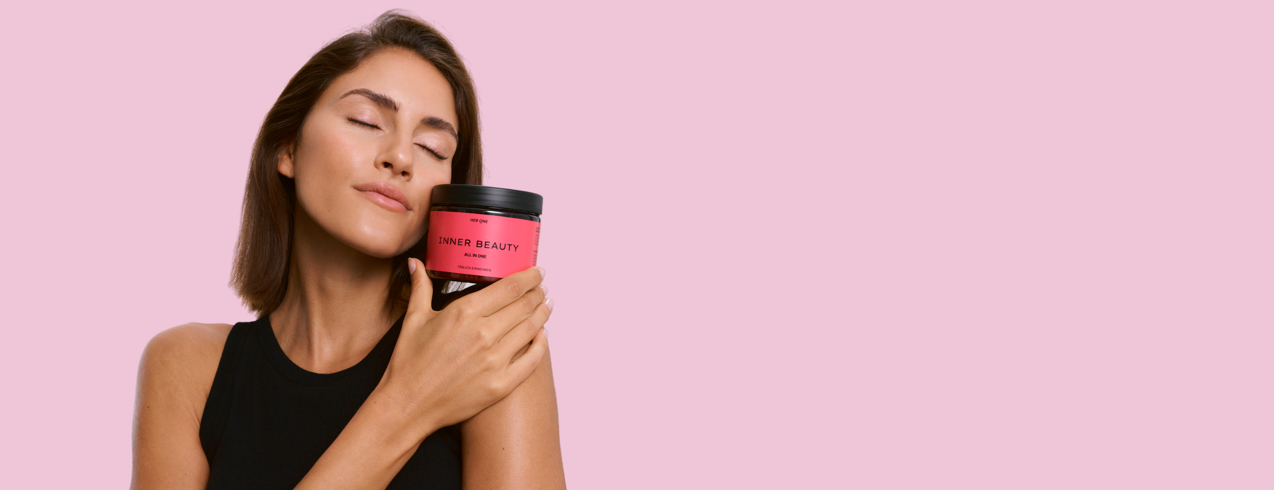 Donna tiene in mano la lattina Inner Beauty sul viso, sfondo rosa, per trasmettere benessere e prosperità