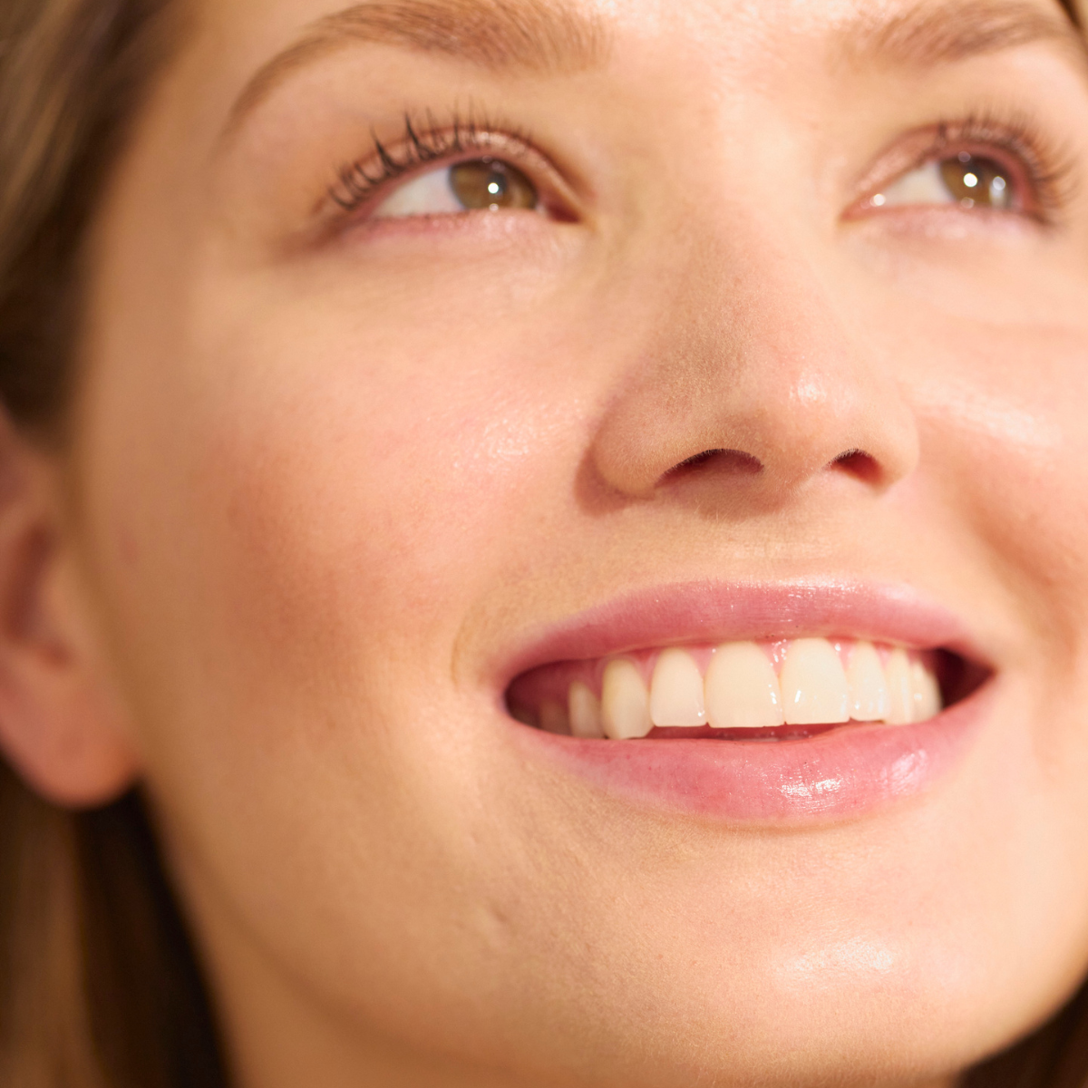 Primo piano di un viso sorridente con pelle luminosa e curata e denti visibili, simbolo di bellezza naturale