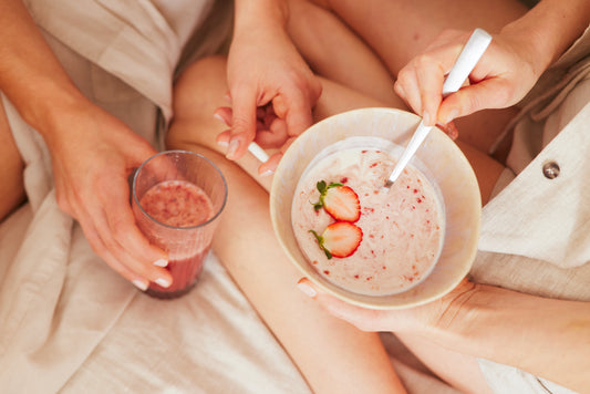 Eén persoon houdt een schaaltje aardbeienyoghurt vast en een ander houdt een glas met roze drank vast.