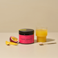 Op de foto zie je INNER BEAUTY All in One met mango-passievruchtsmaak. Naast het product is een in plakjes gesneden mango en een halve passievrucht te zien. De drank wordt gemixt in een glas rechts op de foto en gepresenteerd met een lepel INNER BEAUTY ervoor. 