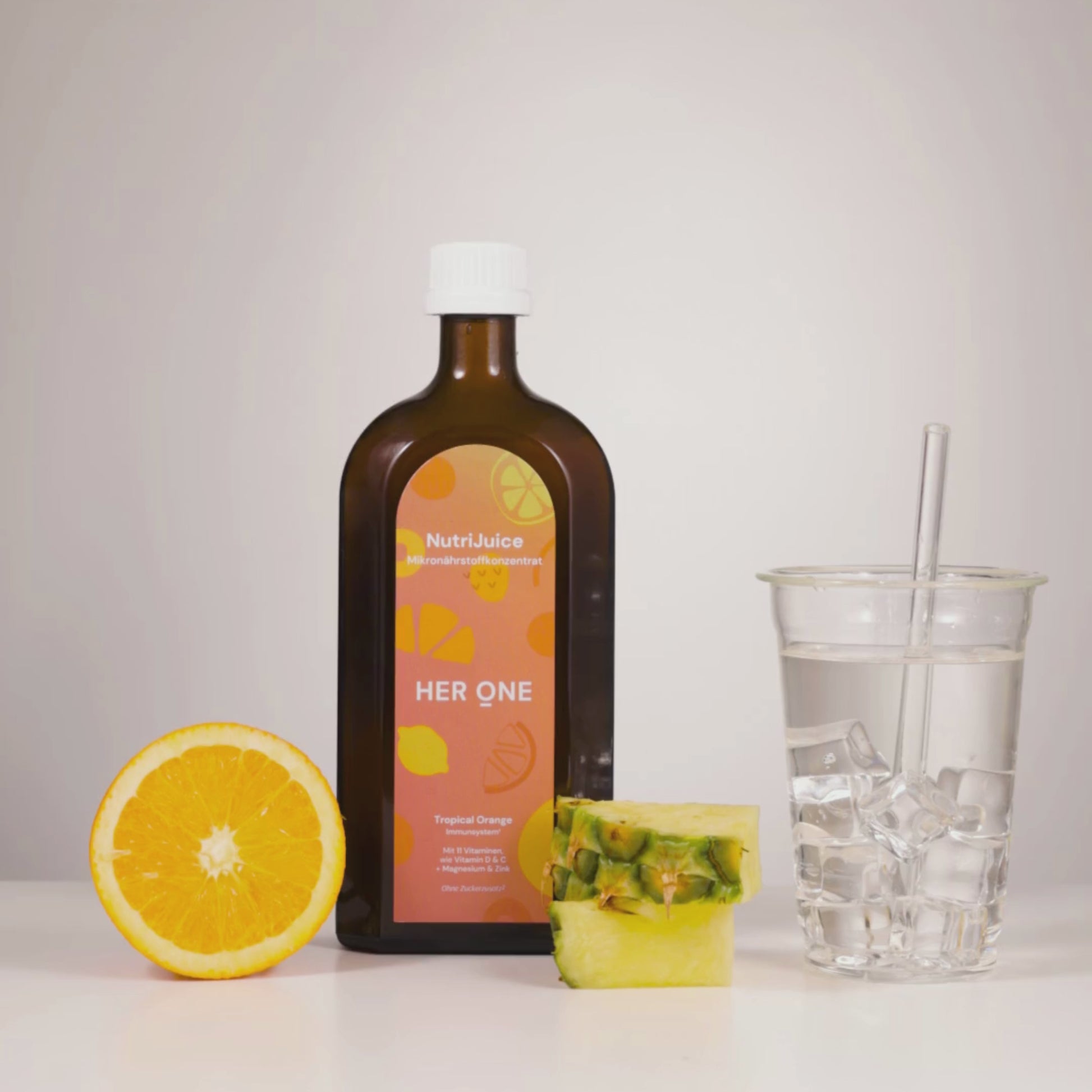 Bruine fles NutriJuice, gehalveerde sinaasappel, ananasstuk en een glas water met ijs op een witte achtergrond.